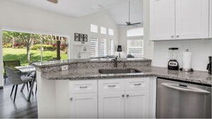 Una cocina moderna con armarios blancos, encimeras de granito, lavavajillas integrado y una licuadora.