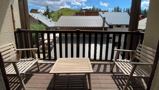 Un terrazzo in legno con tavolo e due sedie, affaccia su una città con edifici e una collina.