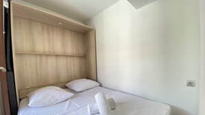 Un letto singolo con biancheria bianca, una testiera in legno e un asciugamano arrotolato sul letto.