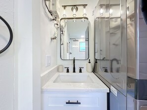 Ein modernes Badezimmer mit einem weißen Waschtisch, einem großen Spiegel und einer integrierten Dusche.