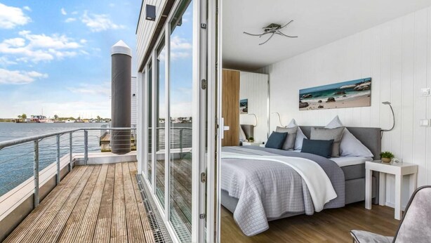 Een slaapkamer met een bed, nachtkastjes, een raam en uitzicht op het water.