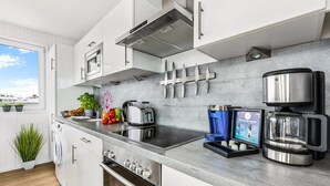 Een moderne keuken met witte kasten, een roestvrijstalen fornuis, een koffieapparaat en een inbouwoven.