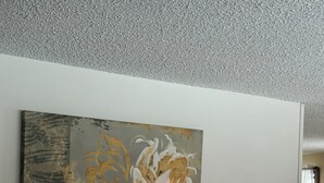 A living room with a large floral painting on the wall, a gray armchair, a lamp, and a table with books and a remote control. - Wellness Gardens Retreat

 (Sidney)