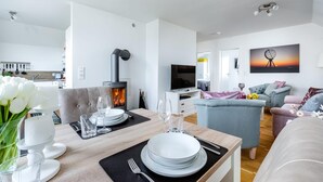 A modern living room with a fireplace, a dining area with a set table, and a cozy seating area with a TV. - Gorgeous apartment in Olpenitz (Olpenitz)