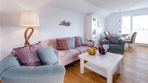 A modern living room with a sofa, a coffee table, and a dining area with chairs and a table. - Gorgeous apartment in Olpenitz (Olpenitz)