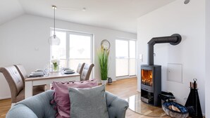 A modern living room with a fireplace, a dining area with a table set for four, and a large window providing natural light. - Gorgeous apartment in Olpenitz (Olpenitz)