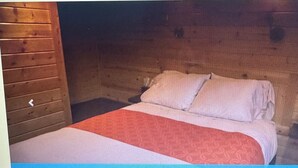 A wooden cabin room with a bed, pillows, and a nightstand. - Charming 2-bedroom cabin in St Mary’s Glacier (Babb)
