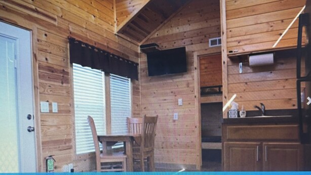 A wooden cabin interior with a door, a window with blinds, a chair, and a shelf with items. - Charming 2-bedroom cabin in St Mary’s Glacier (Babb)