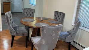 A dining area with a round wooden table and four tufted grey chairs. - Charming 3-bedroom house. (Cortlandt)