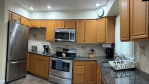 A modern kitchen with wooden cabinets, stainless steel appliances, a granite countertop, and a tiled backsplash. - Charming 3-bedroom house. (Cortlandt)