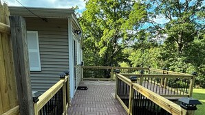 A wooden deck with a patterned floor, surrounded by a wooden fence and a metal railing. - Charming 3-bedroom house. (Cortlandt)