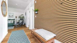 Un salon moderne avec un mur lambrissé en bois, un canapé vert, un fauteuil gris et un tapis à motifs.