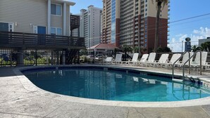 A swimming pool with lounge chairs and a fenced area, surrounded by multi-story buildings.