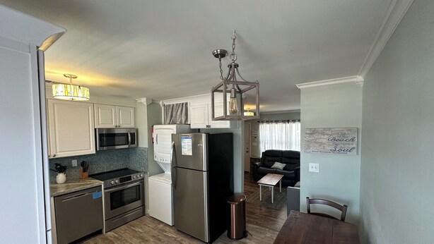 A compact kitchen with modern appliances, a dining area with a wooden table, and a living room with a sofa and a decorative wall piece.