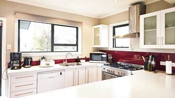 A modern kitchen with white cabinets, a Bosch dishwasher, a microwave, a gas stove, and a window with blinds.