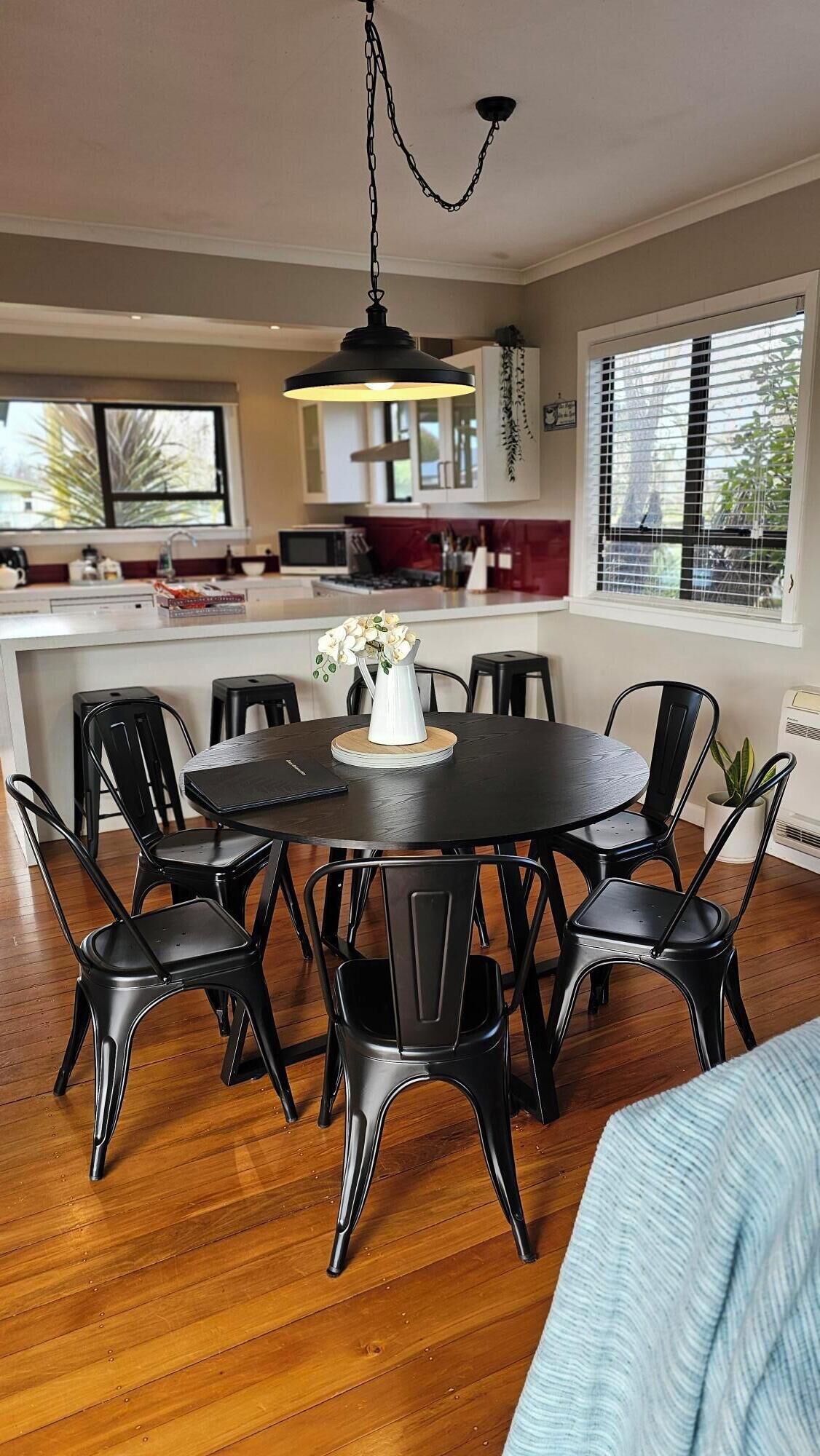 A dining area with a round table, black chairs, and a white vase with flowers.