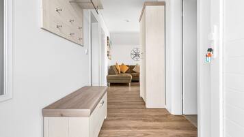 Ein Flur mit einer Holzbänkchen, einer Couch mit Kissen und einer Wandleuchte.