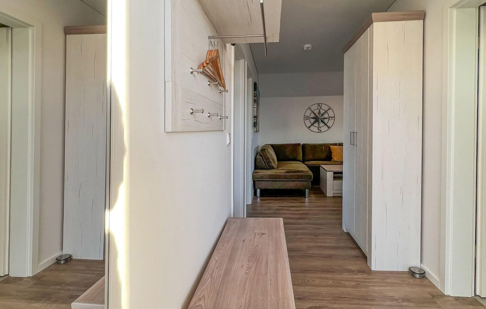 Un couloir avec un banc en bois, des murs blancs et un canapé vert à l’arrière-plan.