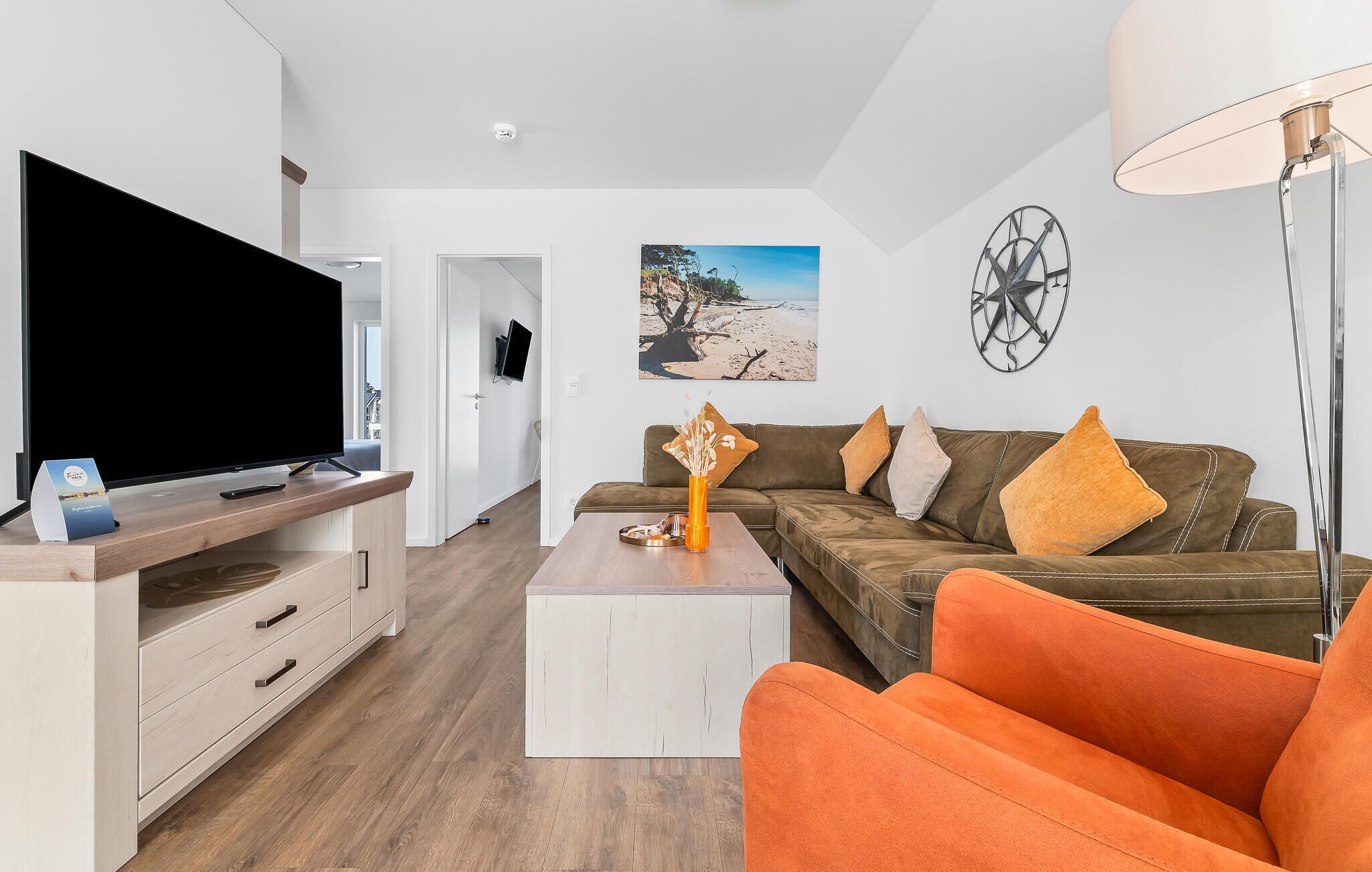 Un salon moderne doté d’un téléviseur à écran plat, d’un ensemble de canapés, d’une table basse et d’une horloge murale.