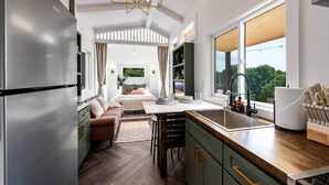 Eine moderne Küche mit integriertem Kühlschrank, Holz Arbeitsplatten, einem Essbereich mit Tisch und Stühlen sowie Blick auf ein Schlafzimmer durch ein großes Fenster.
