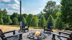 Eine Außenbereich-Sitzgelegenheit mit Adirondack-Stühlen, einer Feuerstelle und Blick auf eine bewaldete Landschaft.