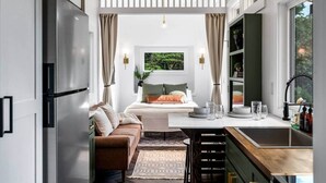 Eine moderne Küche mit Einbaukühlschrank, ein Essbereich mit Holztisch und -stühlen sowie ein gemütliches Schlafzimmer mit Bett und Blick ins Grüne.