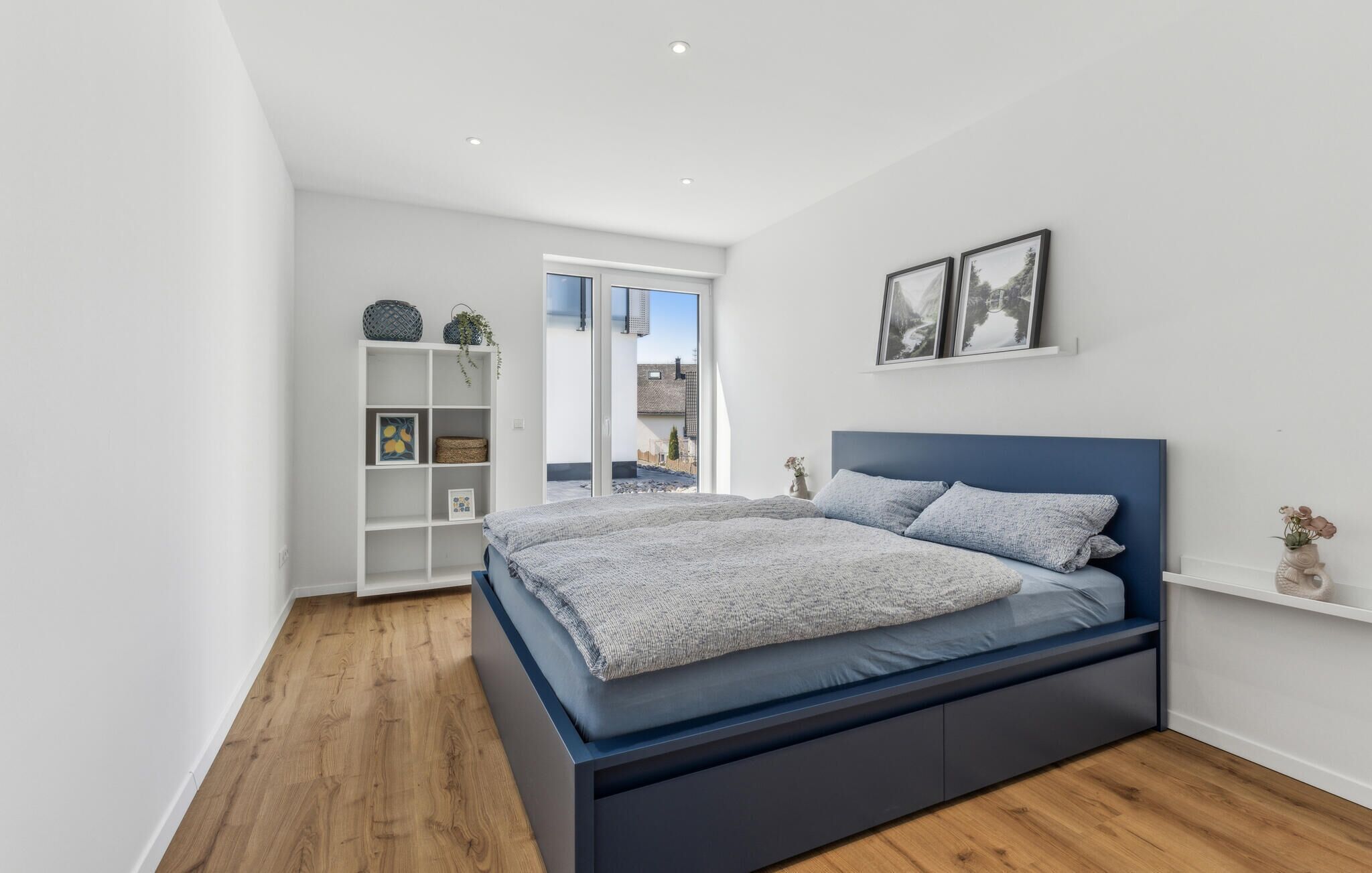 A modern bedroom with a large bed, built-in shelving, and a view of the outdoors.