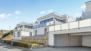 A modern two-story house with a garage, large windows, and a stone retaining wall.