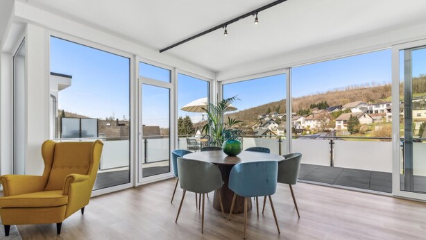 A spacious balcony with a dining table, chairs, and a yellow armchair.