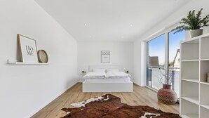 A modern bedroom with a large bed, a cowhide rug, a bookshelf, and a window with a view.