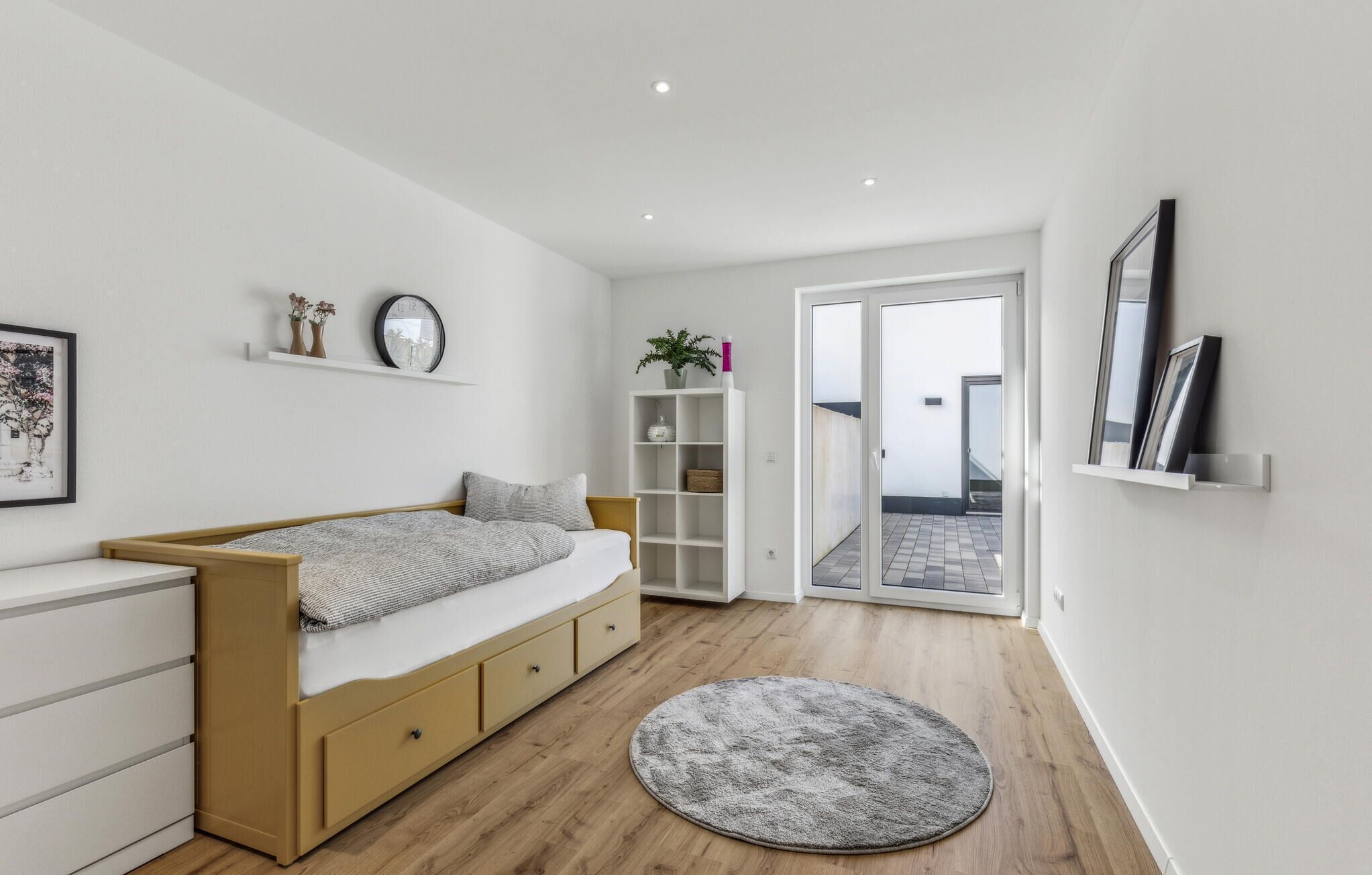 Ein modernes Schlafzimmer mit Bett, Nachttischen, einem Kleiderschrank, einem runden Teppich und einer Schiebetür zum Balkon.