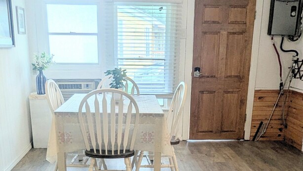 A dining area with a wooden table and chairs, a window with blinds, and a door with a security camera. - 
Lake Sweet Hut by Lake Texoma-B
 (Pottsboro)