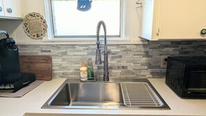 A kitchen with a stainless steel sink, a window with a view, a stone backsplash, and a black appliance on the right. - 
Lake Sweet Hut by Lake Texoma-B
 (Pottsboro)