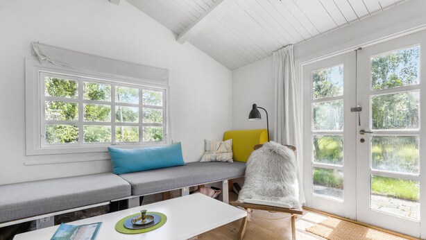 A bright room with a large window, a bench with cushions, a small table with a lamp, and a door with multiple windows. - 2 bedroom lovely home in Jægerspris (Jægerspris)