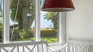 A room with a white chair, a table, and a window with a view of greenery and a body of water. - 2 bedroom lovely home in Jægerspris (Jægerspris)