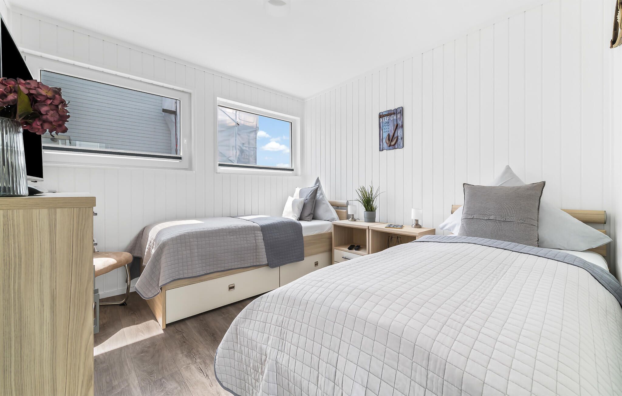 A bedroom with two beds, a desk, a chair, a dresser, a window, and a plant.