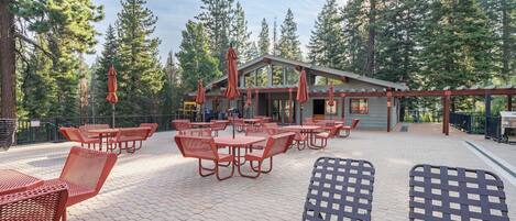 An outdoor seating area with tables and chairs, surrounded by trees.