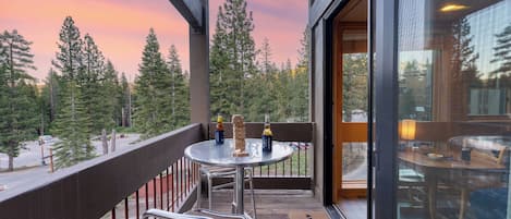 A balcony with a table, chairs, and a view of trees and a sunset.