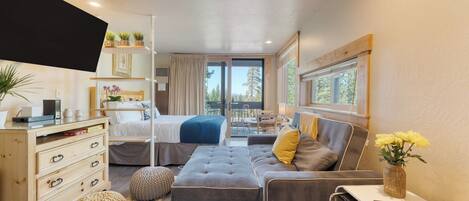 Un dormitorio pequeño con cama, sofá, escritorio y ventana con vistas a árboles.