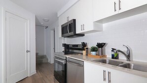 Une cuisine moderne avec des armoires blanches, des appareils en acier inoxydable et un plancher en bois.