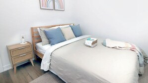 Une chambre bien rangée, avec un lit, une table de chevet et des œuvres d’art accrochées au mur.
