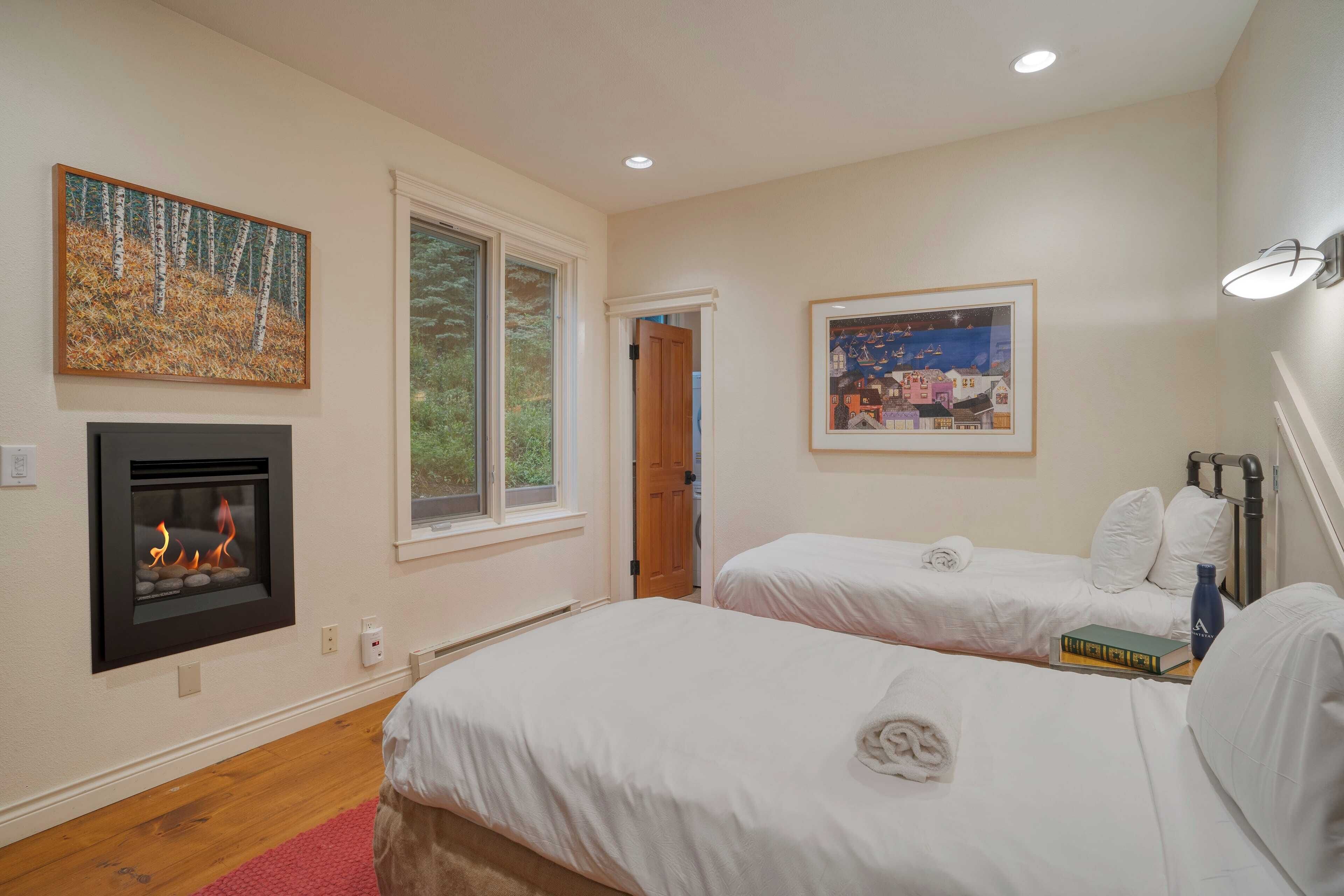 A bedroom with two beds, a fireplace, and two framed pictures on the walls.