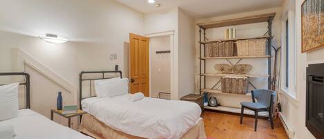 A bedroom with two beds, a bookshelf, a chair, and a fireplace.