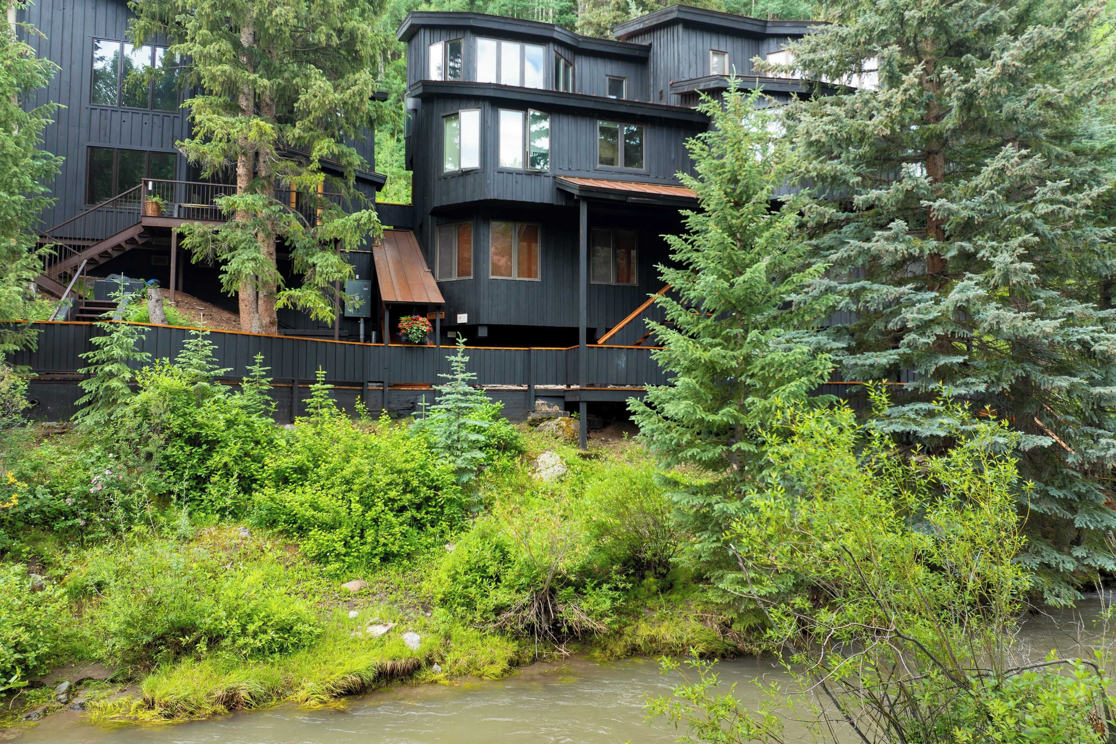 A multi-story building with a wooden exterior, surrounded by dense greenery and a small stream.