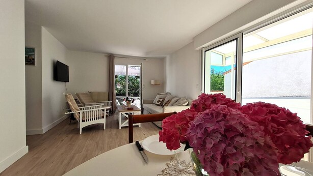 A modern living room with a white sofa, a white armchair, a small table with a vase of flowers, and a TV mounted on the wall. - Saint Georges de Didonne - IDEAL NEIGHBOURHOOD FOR RESOURCE - RENOVATED HOUSE (ST GEORGES DE DIDONNE)