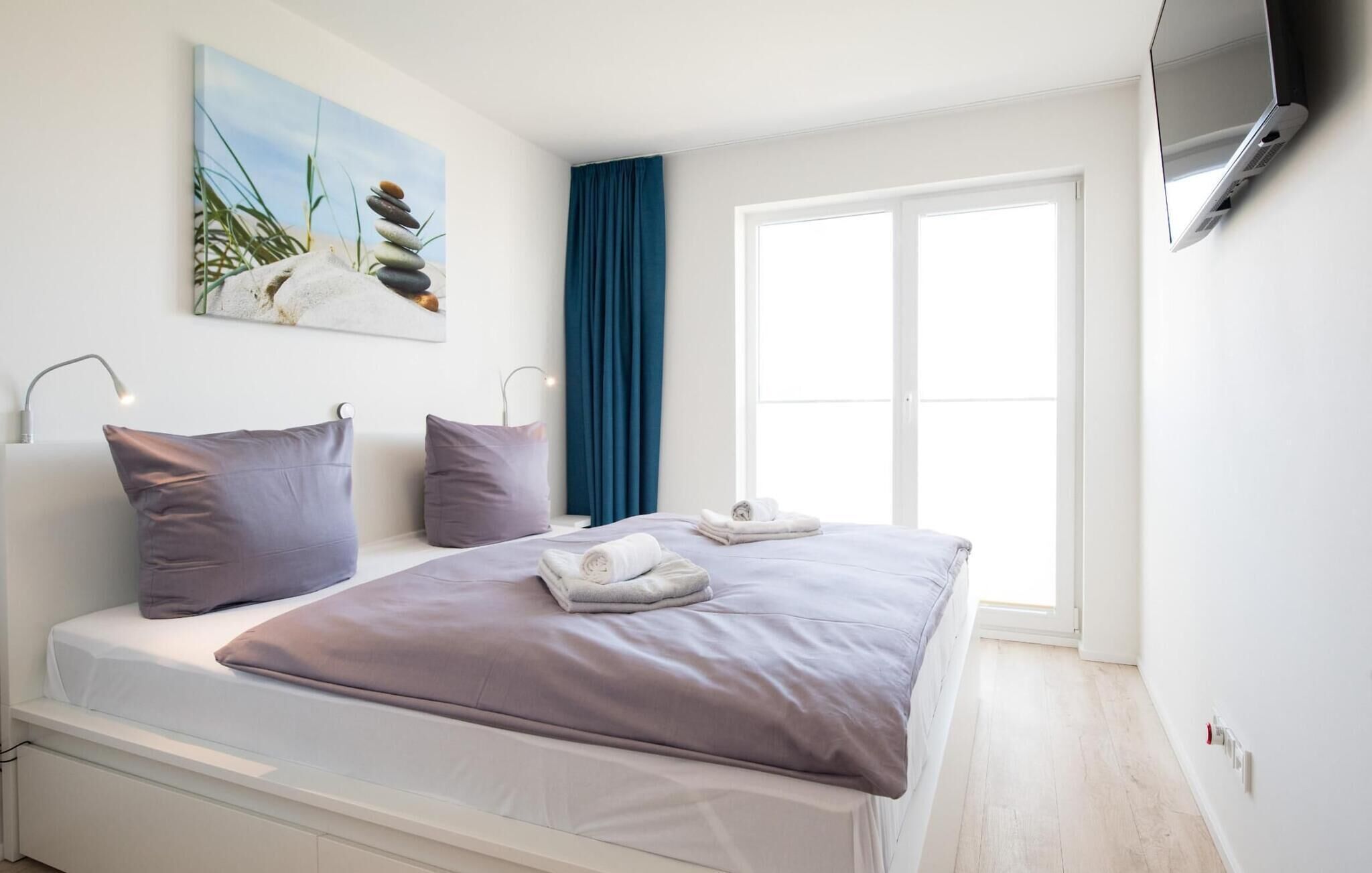 A modern bedroom with a bed, pillows, a painting, a window, and a TV.