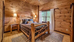 Une chambre à coucher dans une cabane en bois, avec un lit, des tables de chevet et une fenêtre avec des rideaux.