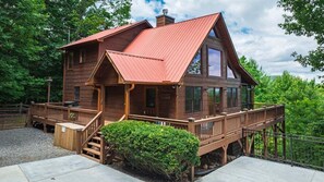 Un chalet rustique avec un toit rouge, une terrasse en bois et un escalier menant à l’entrée.