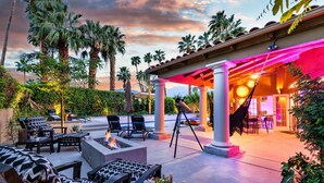 An outdoor patio area with lounge chairs, a fire pit, and a covered seating area with a view of the pool and palm trees. - Amazing- Ultra Luxe Estate, Resort like Pool, Firepit & More (Palm Springs)