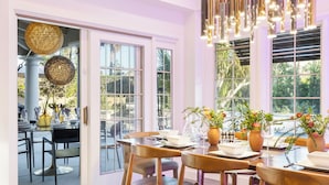 A dining area with tables set for service, large windows with views of greenery, and hanging pendant lights. - Amazing- Ultra Luxe Estate, Resort like Pool, Firepit & More (Palm Springs)
